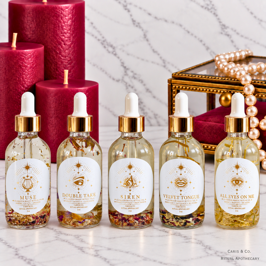 Five glamour magic ritual oils labeled Muse, Siren, Double Take, All Eyes on Me, Velber Tongue next to a gold and red jewlery box.
