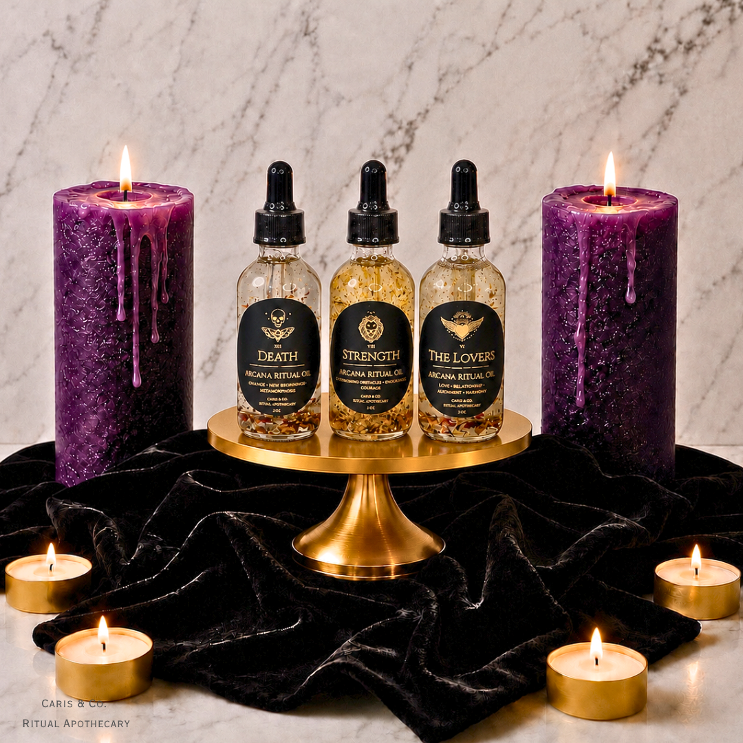 Three amber glass dropper bottles labeled Death, Strength, and The Lovers sit on a gold pedestal, flanked by two large purple wax candles and small tealight candles on a black velvet cloth against a marble background.  Caris & Co. Ritual Apothecary