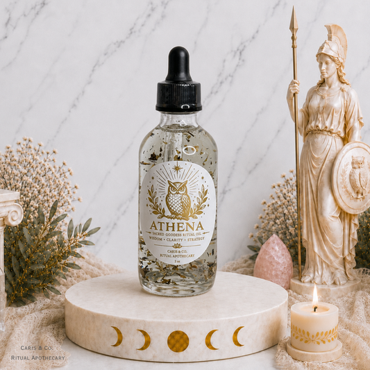 A clear glass dropper bottle labeled ATHENA Ritual oil by Caris & Co. Ritual Apothecary, filled with clear oil and suspended botanicals, displayed on a cream marble pedestal. 