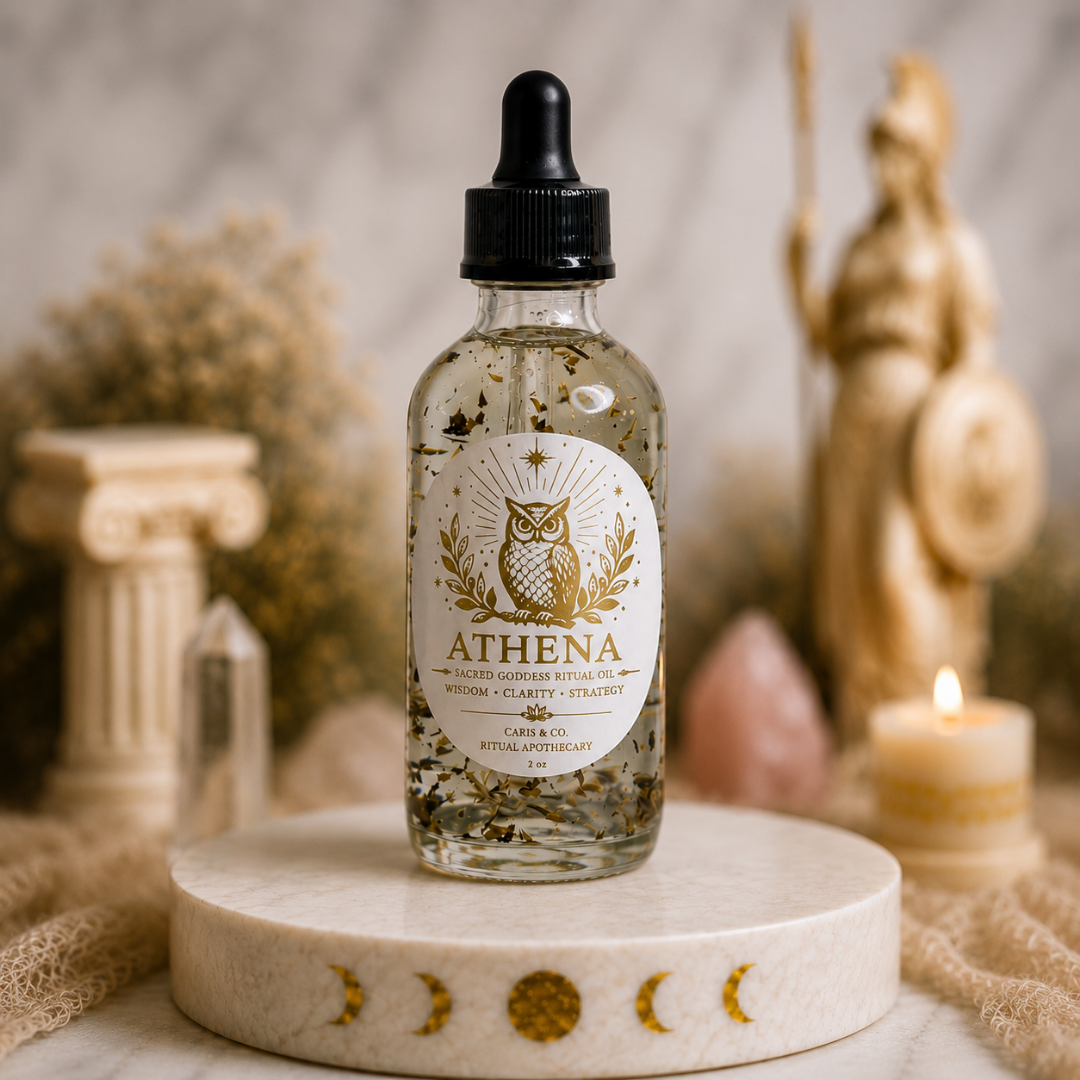 A clear glass dropper bottle labeled ATHENA Ritual Oil stands on a round stone pedestal.  Caris & Co. Ritual Apothecary