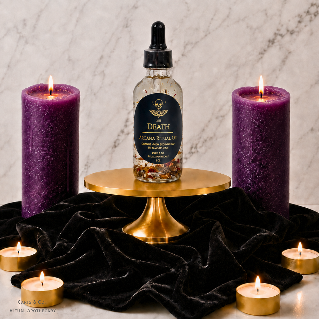 A bottle of Death Arcana Ritual Oil is displayed on a gold pedestal, flanked by two large purple pillar candles and several small tealight candles on a black velvet cloth against a marble background.  Caris & Co. Ritual Apothecary