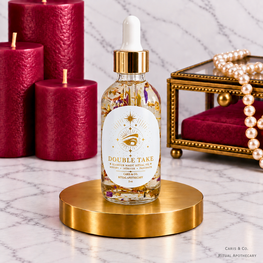 Caris & Co. Double Take glamour magic ritual oil bottle with red candles and pearl jewelry on a marble background.