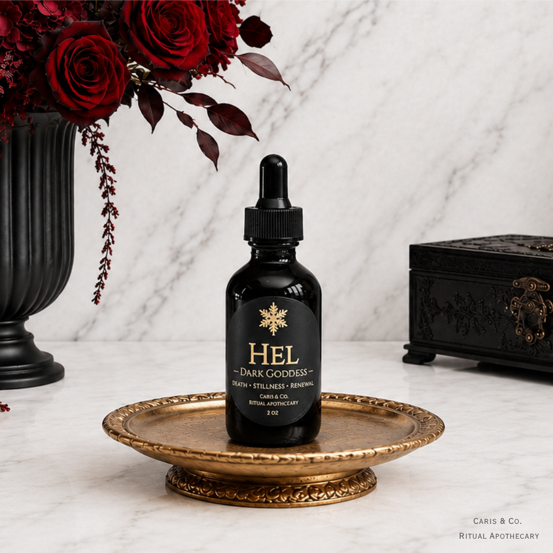 A 2 oz black glass dropper bottle of 'Hel - Dark Goddess' ritual oil by Caris & Co. Ritual Apothecary, displayed on an ornate gold tray.