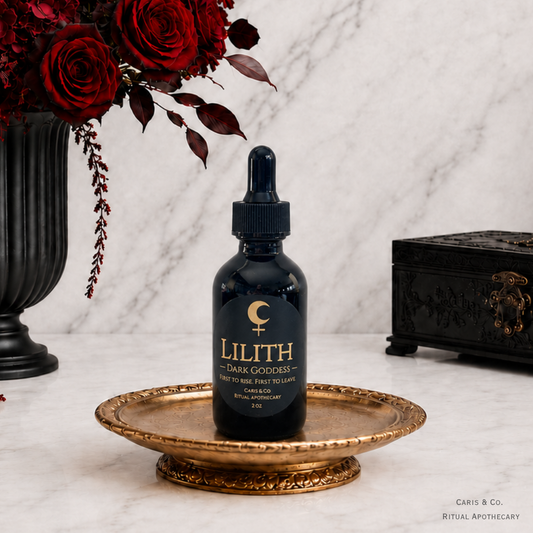 A dark glass dropper bottle labeled 'LILITH DARK GODDESS' sits centered on an ornate gold tray against a white marble background, with red roses in a black vase on the left and a black decorative box on the right.  Caris & Co. Ritual Apothecary