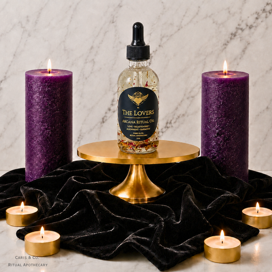 A bottle of 'The Lovers' Arcana Ritual Oil by Caris & Co. Ritual Apothecary is displayed on a gold pedestal, flanked by two large purple pillar candles and four small tealight candles on a black velvet cloth against a marble background.