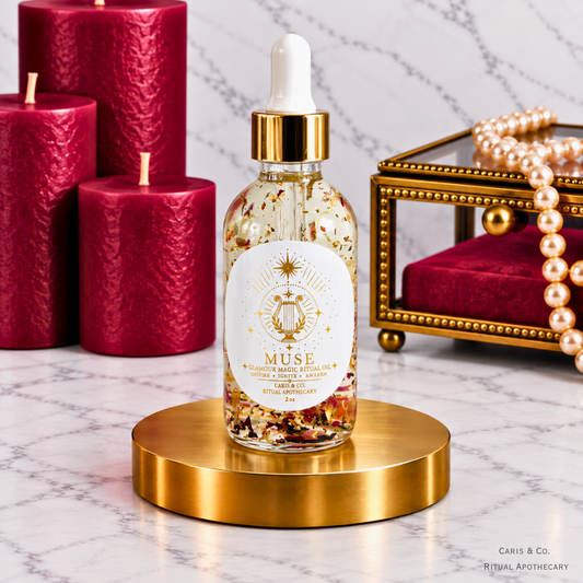Caris & Co. Muse glamour magic ritual oil bottle with red candles and pearl jewelry on a marble background.