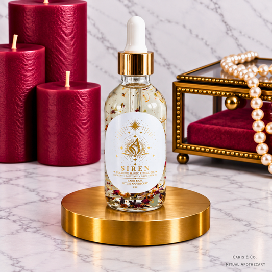 Caris & Co. Siren glamour magic ritual oil bottle with red candles and pearl jewelry on a marble background.