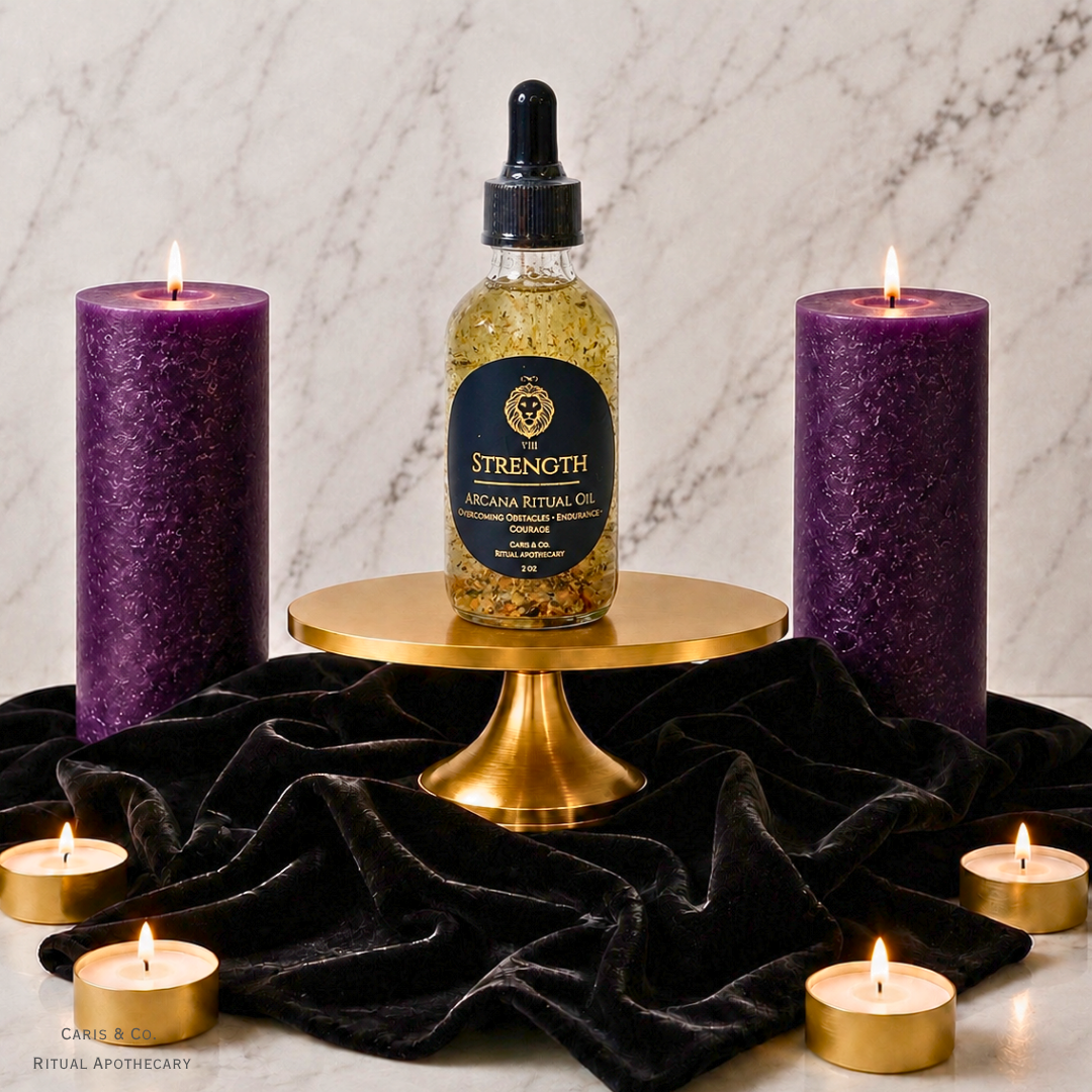 A bottle of 'Strength' Arcana Ritual Oil sits on a gold pedestal, flanked by two large purple pillar candles and small tealight candles on a black velvet cloth against a marble background.  Caris & Co. Ritual Apothecary