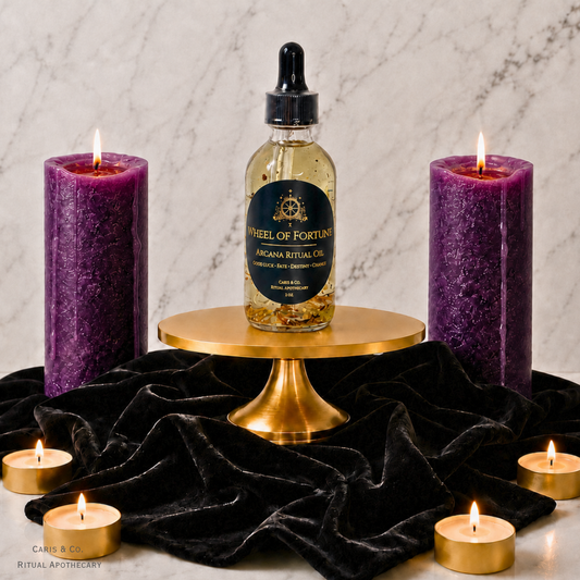 A bottle of Wheel of Fortune Arcana Ritual Oil by Caris & Co. Ritual Apothecarysits on a gold pedestal, flanked by two large purple pillar candles and surrounded by small tealight candles on a black velvet cloth against a marble background.